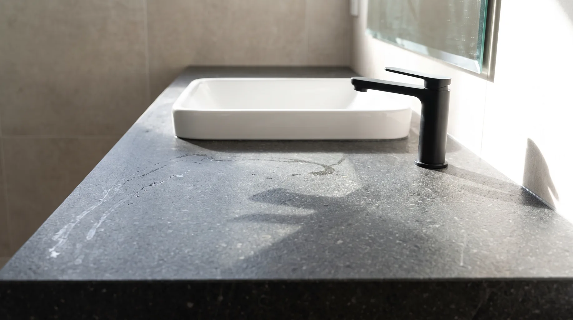 Close-up of a matte black single-lever basin mixer tap set into a dark basalt stone worktop in a finished Bracknell bathroom vanity, bright directional natural light.
