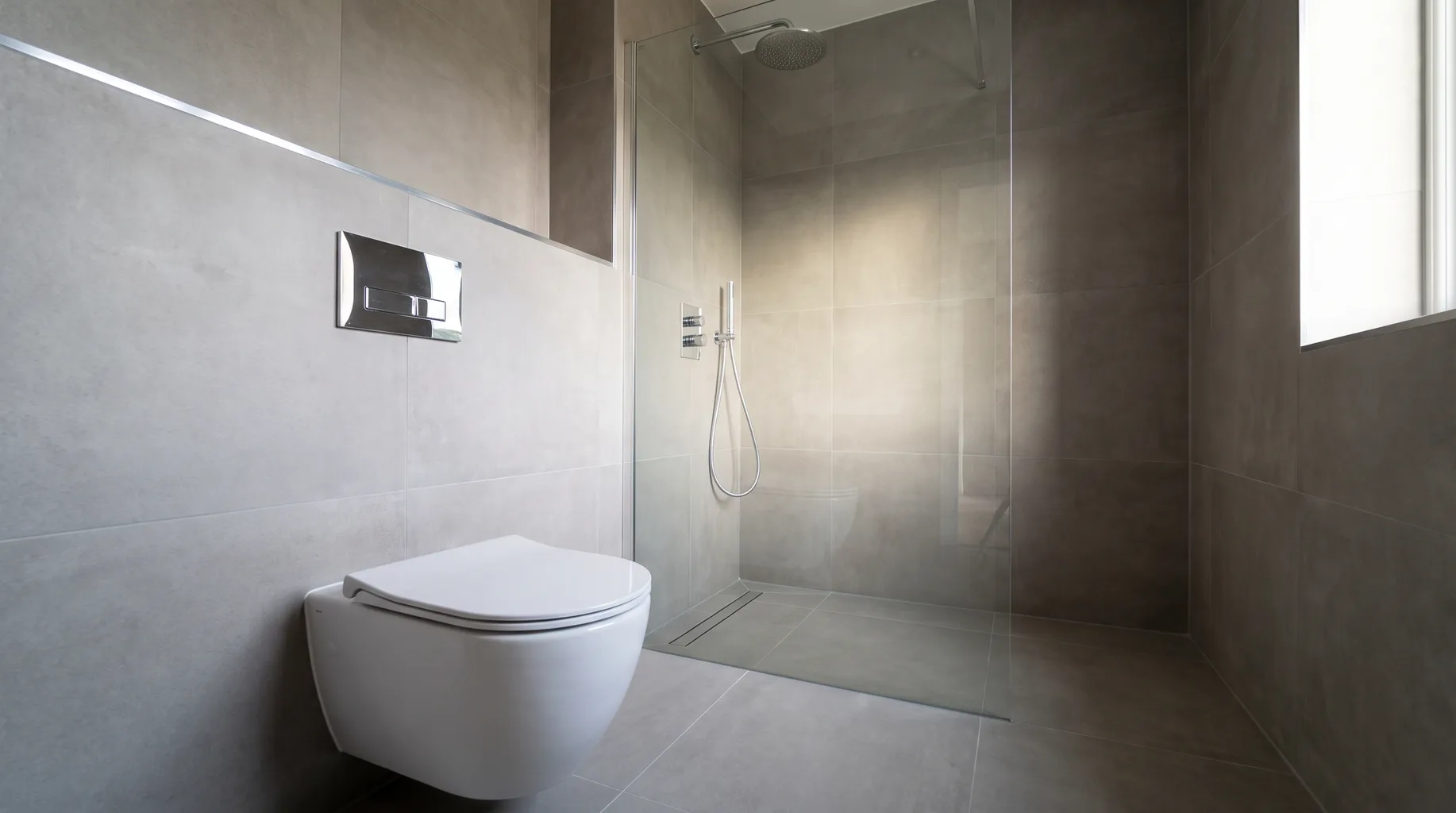 Finished bathroom with a wall-hung WC and concealed thermostatic shower system beyond
