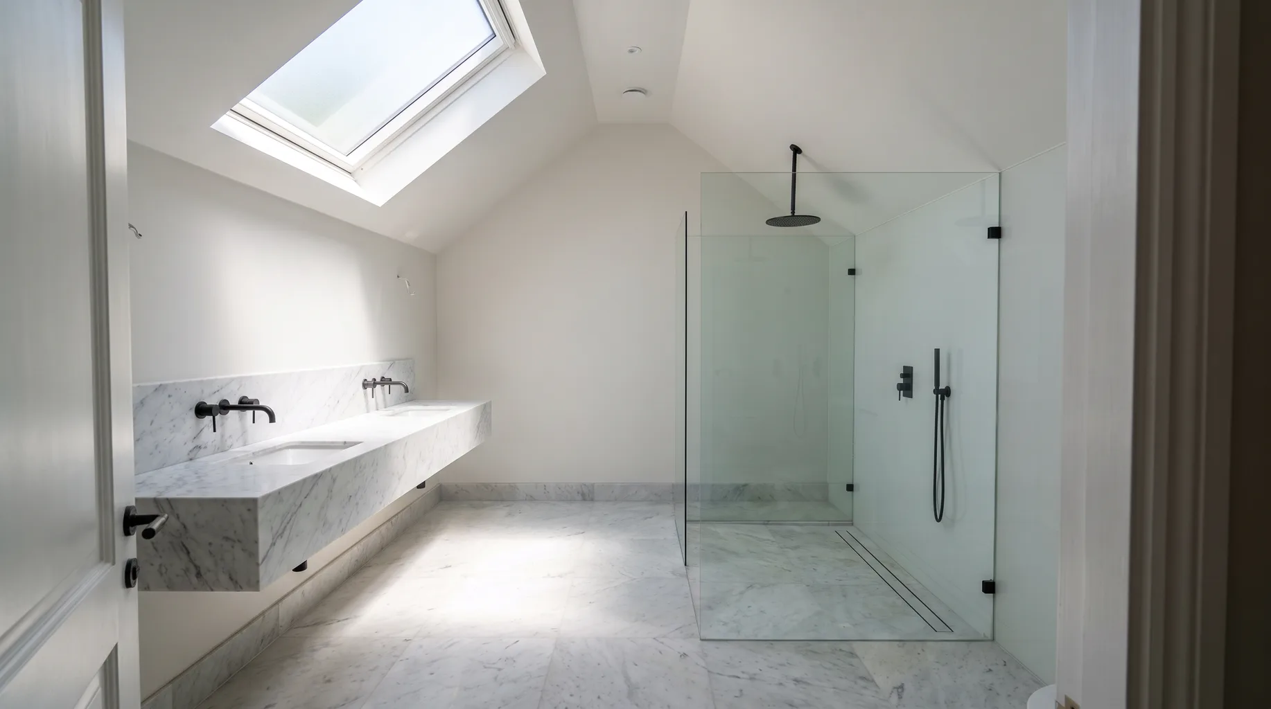 A finished Virginia Water wet room with honed Calacatta marble floor, matte black shower fittings and a long floating stone double vanity, bright midday skylight above.