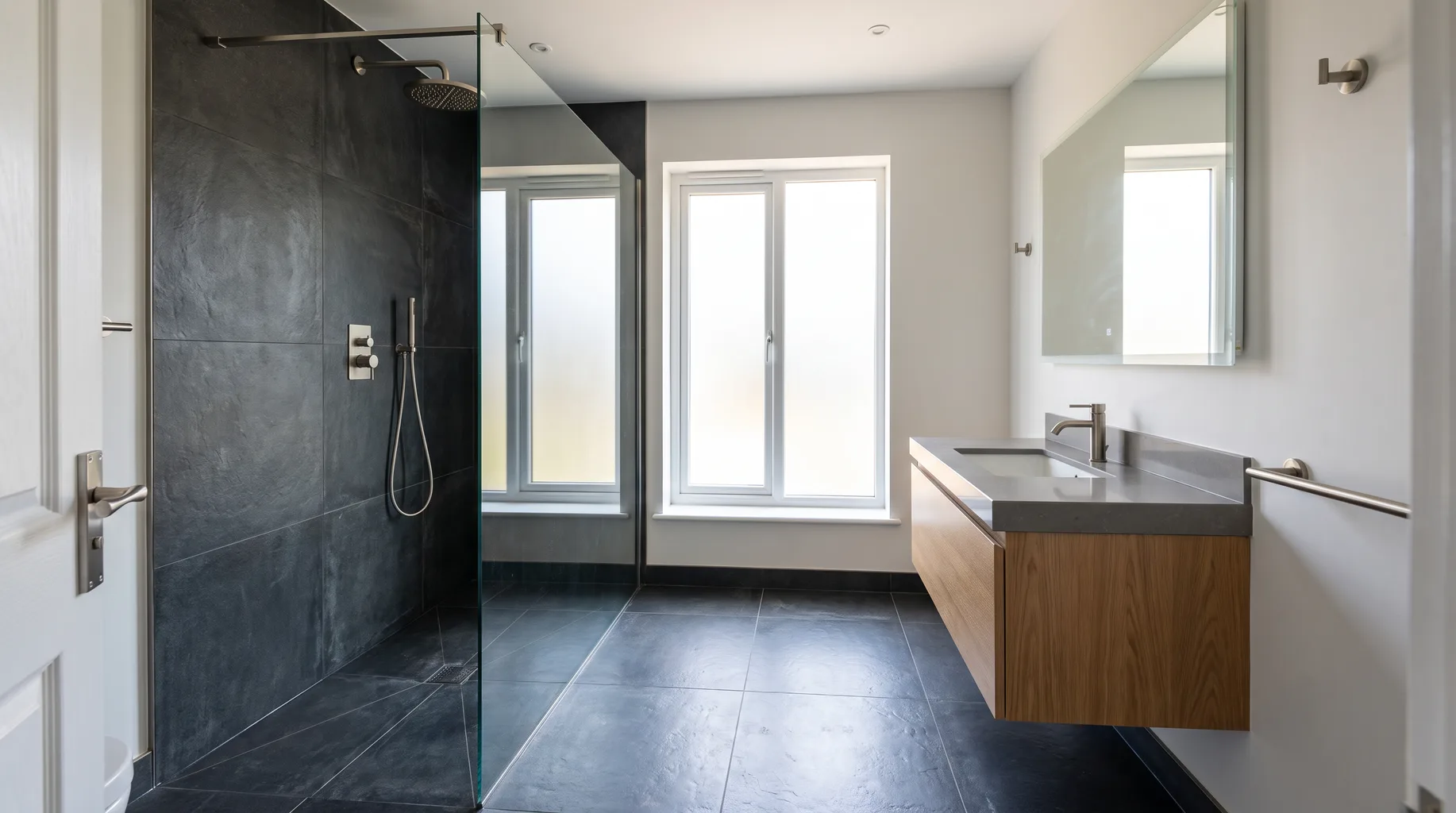 A finished Warfield family bathroom with a large walk-in shower enclosure and wall-mounted basin, dark basalt-effect porcelain floor and brushed nickel fittings, under bright daytime light.