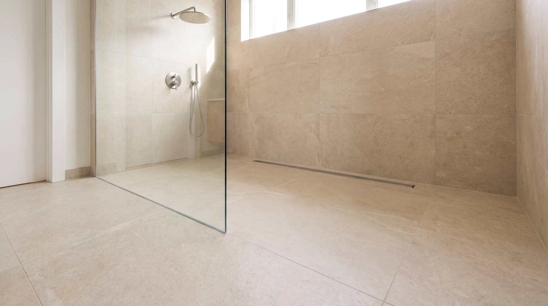 Finished luxury wet room with continuous large format porcelain flooring, linear drain and glass panel, showing the open barrier-free finish of a true wet room