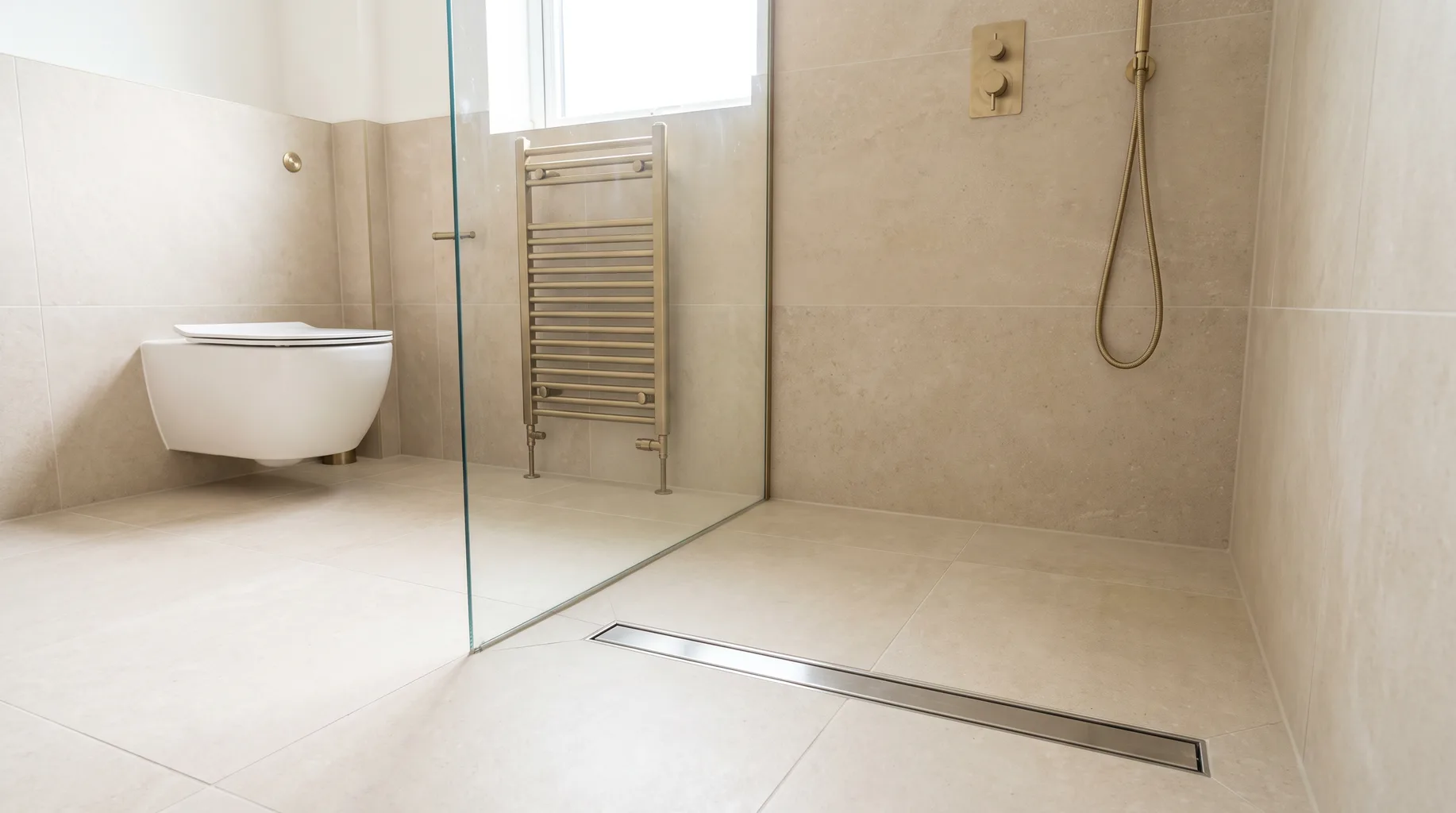Finished level-access wet room with seamless tiled floor, linear drain and half-height glass panel