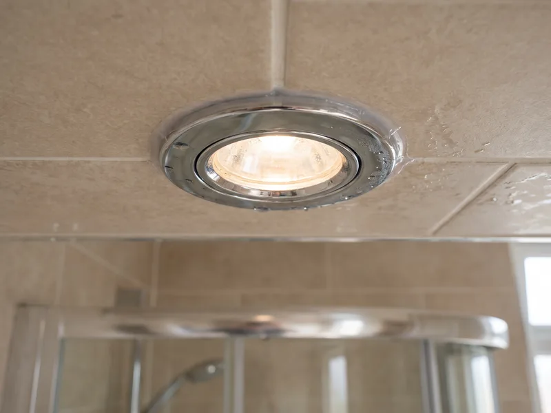 Close detail of a shower-rated recessed downlight set into a finished tiled ceiling above a walk-in shower