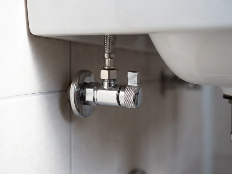 Macro detail of a chrome isolation valve fitted beneath a basin, allowing future servicing without draining the whole system