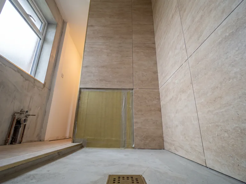 Shower recess mid-tiling with large-format travertine-toned porcelain tiles partly laid over a freshly tanked waterproof membrane