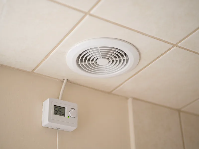 Close detail of a flush ceiling extract grille and wall-mounted humidistat control in a finished bathroom