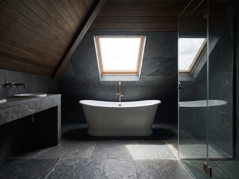 Finished bathroom built into a loft conversion with a sloped ceiling following the roofline and a freestanding bath beneath it