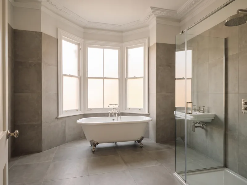 Finished luxury Victorian-style bathroom with a roll-top freestanding bath beneath a bay window in Camberley