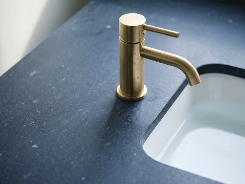 Close detail of a brushed brass single-lever basin tap on a navy stone vanity countertop