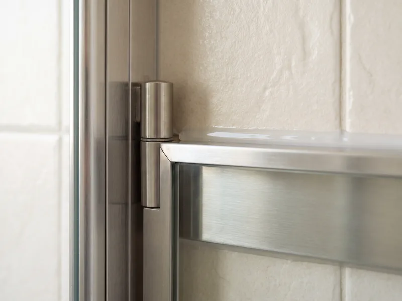 Close-up of a framed shower screen's metal profile and hinge against tiled wall