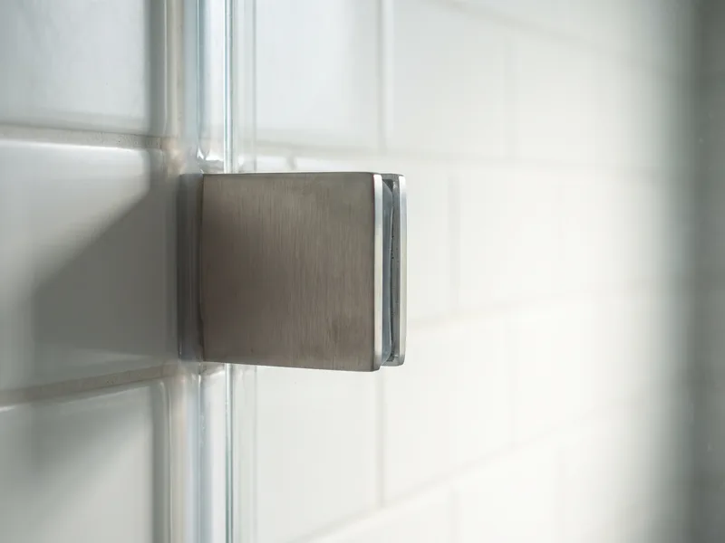 Close-up of a frameless shower screen's thick glass edge and minimal wall bracket against tiled wall