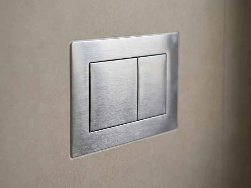 Close-up of a brushed chrome dual-flush plate set flush into large-format porcelain tiling