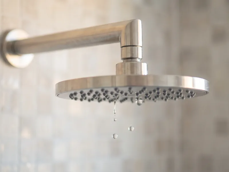 Close-up of a round overhead rainfall shower head with water droplets caught mid-fall