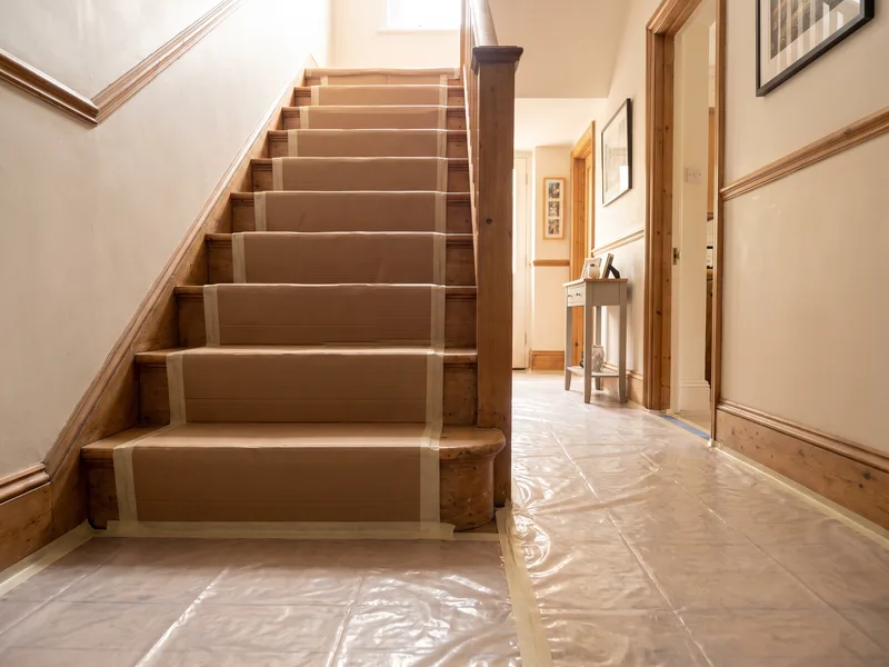 Staircase and hallway protected with boards and taped dust sheets ahead of a bathroom installation elsewhere in the house