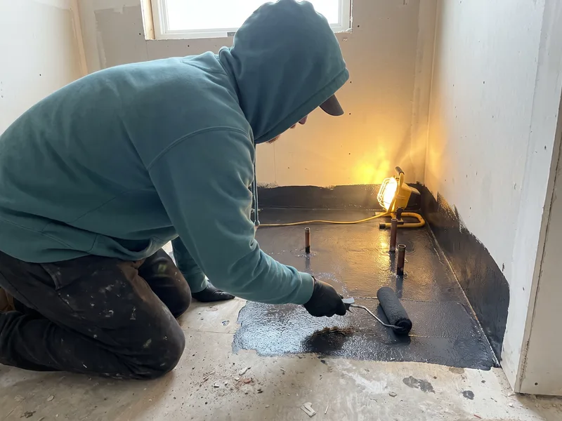 Installer rolling liquid tanking membrane onto a shower floor during the boarding and waterproofing stage of a bathroom installation