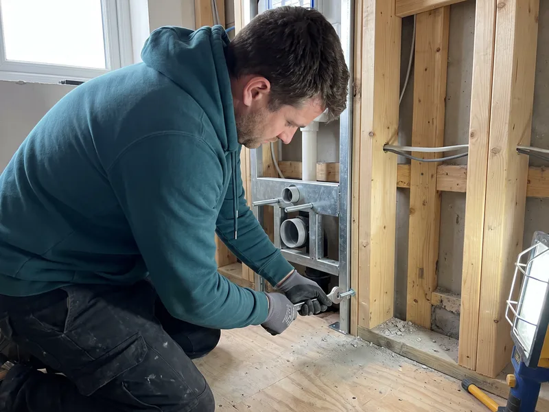 Installer bolting a wall-hung WC carrier frame to the floor and wall structure at first fix