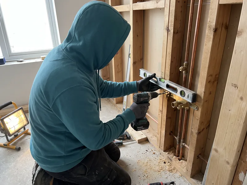 Installer levelling a wall-mounted pipe bracket at first fix for exposed Lefroy Brooks brassware