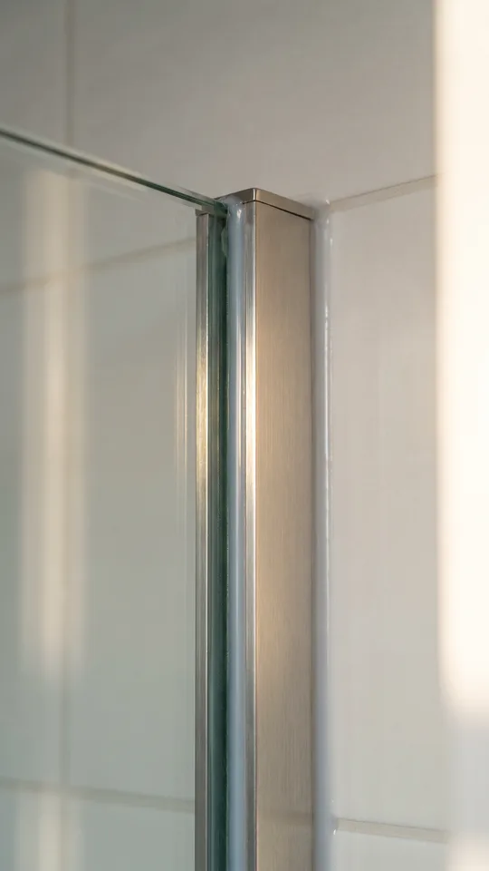 Macro close-up of the edge of a frameless Matki glass shower screen held by a slim metal wall clamp