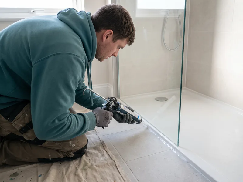 Installer applying a silicone sealant bead along the base of a newly fitted Matki glass shower screen