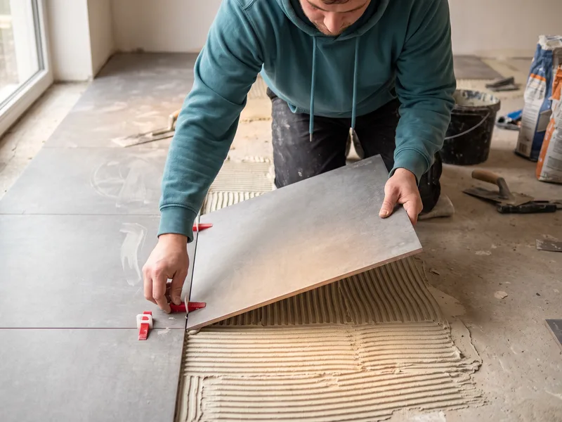 Installer pressing a large-format porcelain floor tile into adhesive and inserting a levelling clip