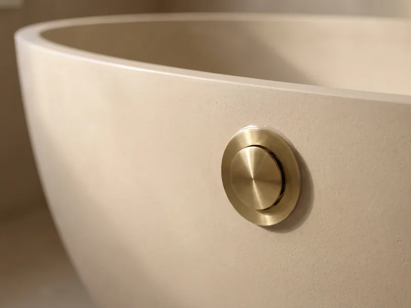 Close detail of a brushed brass overflow and waste fitting on a freestanding bath