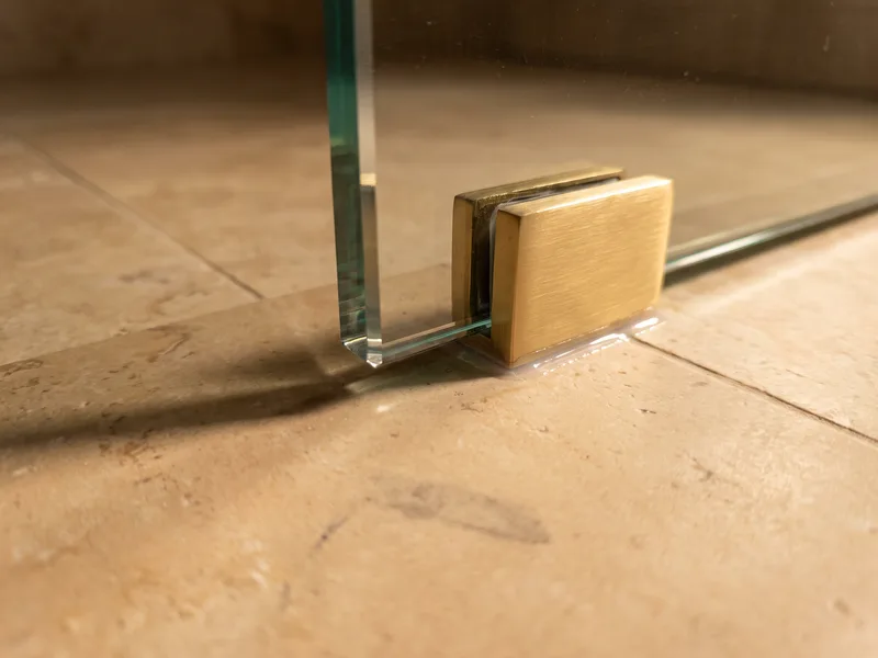 Close detail of a frameless glass shower screen's polished edge held by a brushed brass clamp bracket