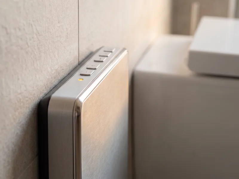 Close detail of a shower toilet's side control panel beside the WC pan, finished and ready for commissioning