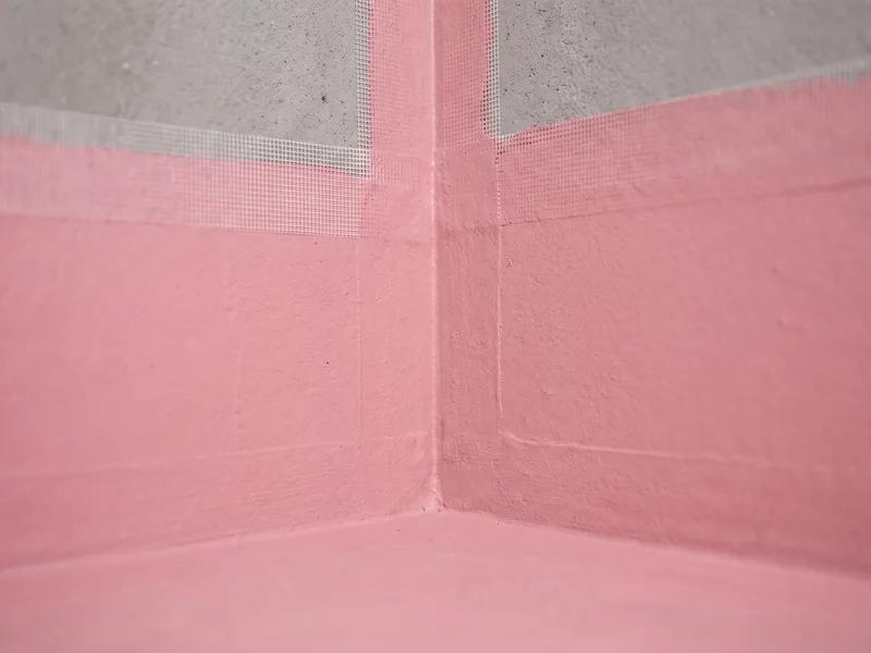 Macro detail of a fully cured liquid waterproofing membrane with reinforcing fabric tape embedded at an internal corner, ready for tiling