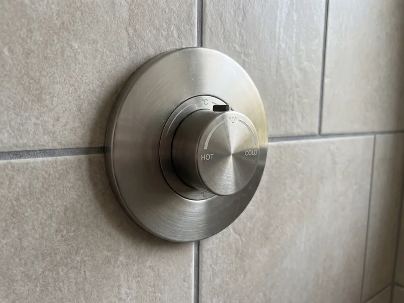 Close-up of a round wall-mounted thermostatic shower valve with a single temperature dial