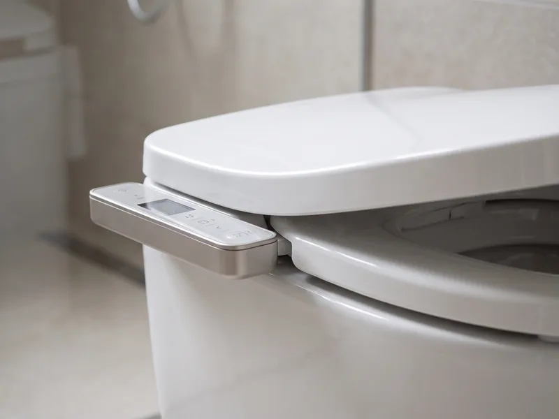 Close-up of an integrated shower toilet unit's ceramic seat and control panel