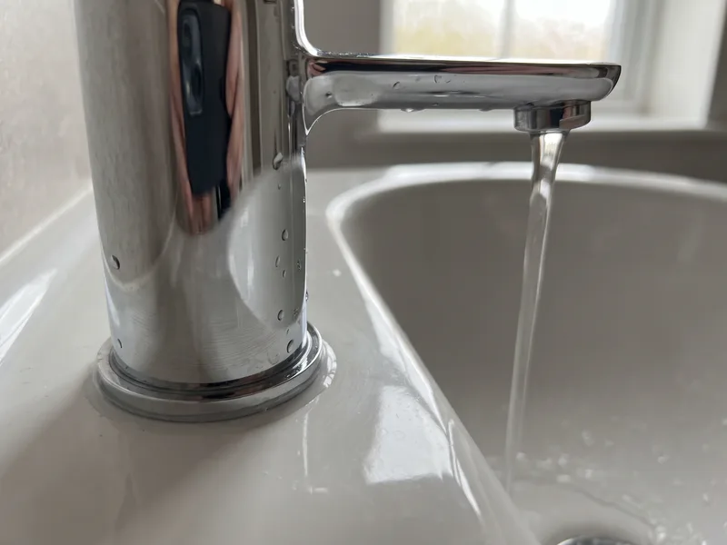 Close-up of a polished chrome basin mixer tap with water running, finished Twyford bathroom detail