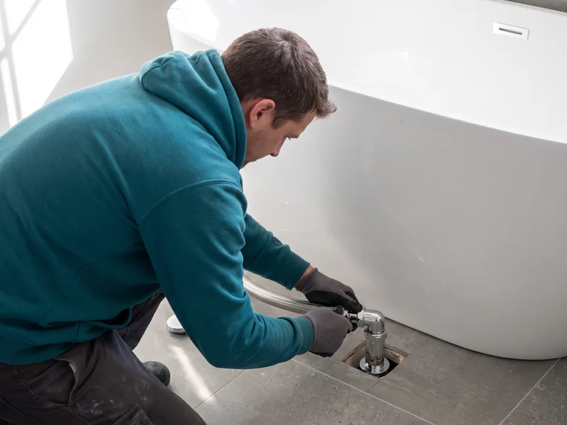 Installer connecting a floor-mounted waste pipe beneath a positioned freestanding Victoria + Albert bath