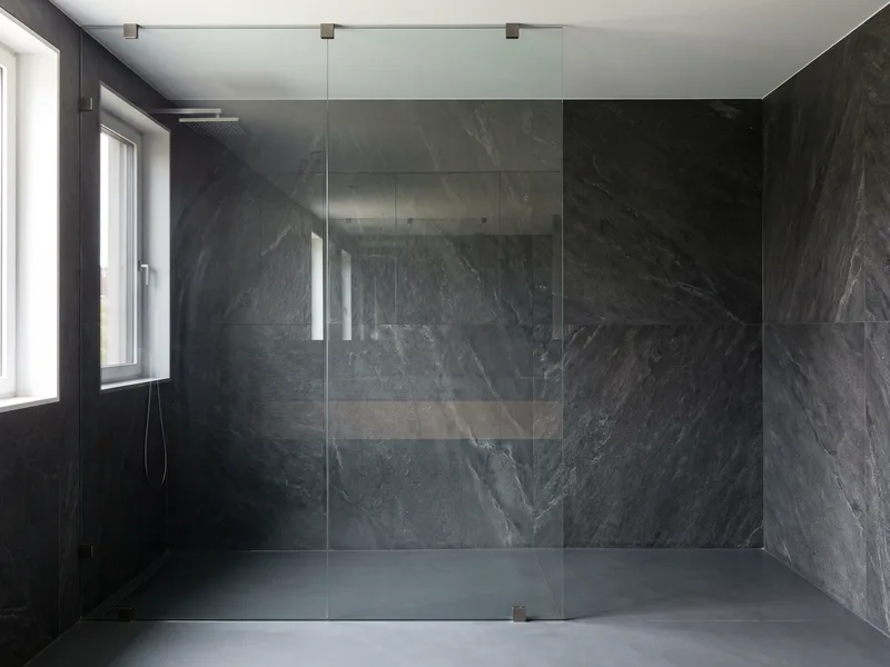 Frameless glass shower panel against an anthracite stone wall forming an open walk-in shower zone