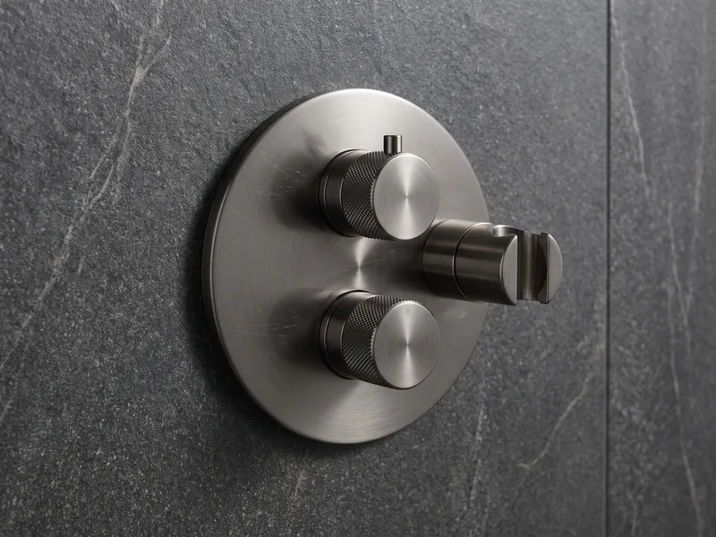 Close detail of a brushed gunmetal concealed thermostatic shower valve and handset on an anthracite stone wall