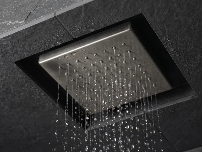 Close detail of an overhead rainfall shower head with water falling, set into an anthracite stone ceiling recess