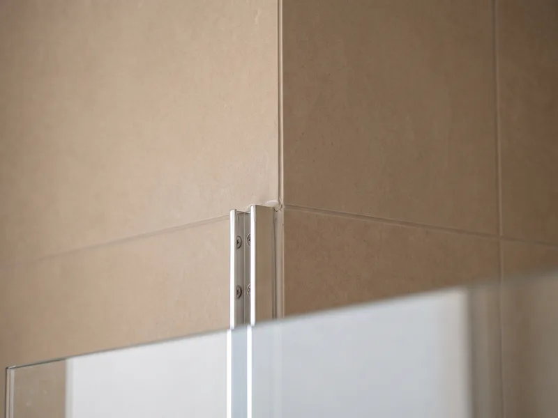 Close-up of a tiled internal corner behind a fixed glass shower panel with the wall channel fixing visible