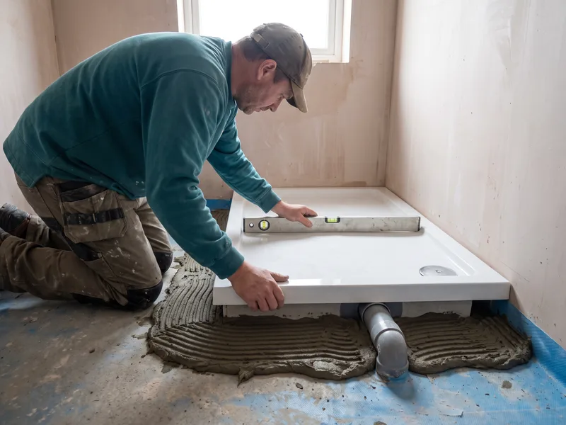 Installer levelling and bedding a low-profile shower tray in a mortar bed, checking with a spirit level before wall tiling begins