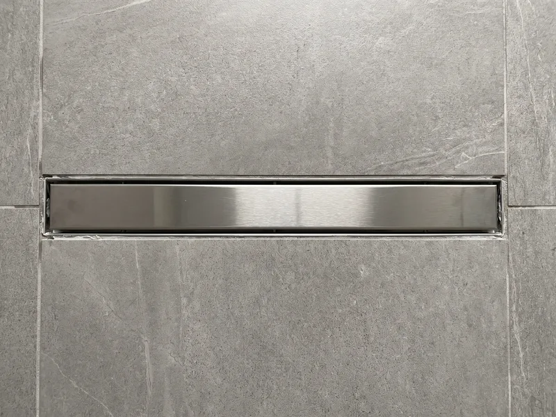 Overhead close-up of a brushed steel linear drain channel set flush between rows of large-format porcelain tile