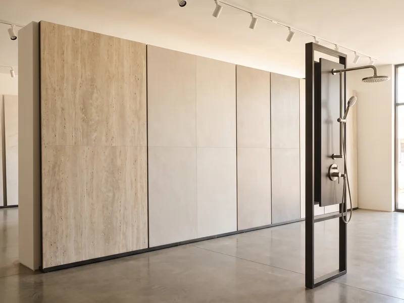 Showroom display wall of porcelain and natural stone tile samples alongside a brushed nickel shower head