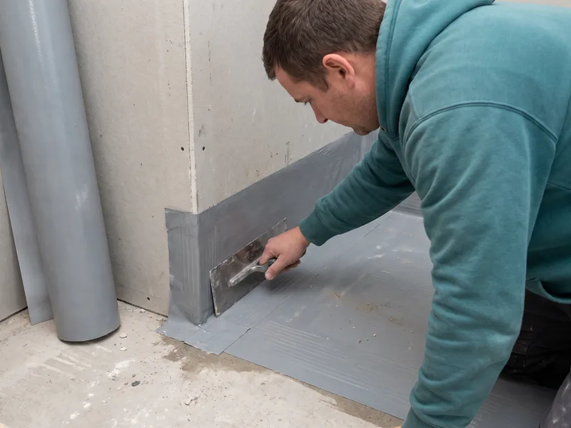 Installer pressing a waterproofing membrane into a floor-to-wall corner before tiling in a Windsor period property