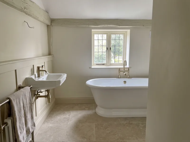 Finished luxury bathroom in an older Winkfield Row cottage with a freestanding roll-top bath under a small-paned window