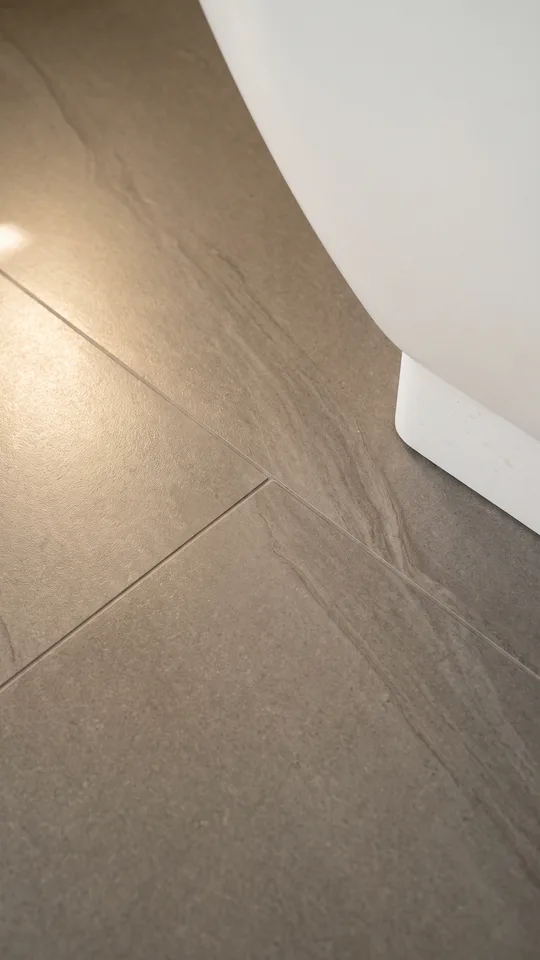 Close-up of honed natural stone floor tiles meeting at a precise mitred corner beside a freestanding bath plinth